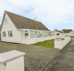 A white house with a tiled roof and a long enclosed porch with windows along the front at Ty Taid in Rhosneigr