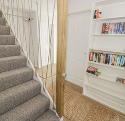 A carpeted staircase next to a bookshelf with books and dvds in a hallway with two white doors at Ty Taid in Rhosneigr
