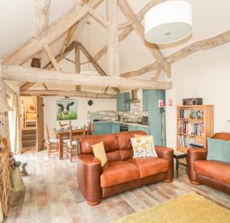 A living room and kitchen area with exposed wooden beams two brown leather sofas and a dining table at Megs Cottage in Tiddington