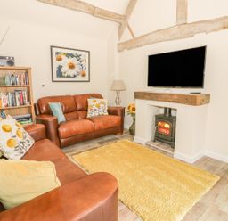 A living room with brown leather sofas a yellow rug a wood burning stove and a bookshelf at Megs Cottage in Tiddington