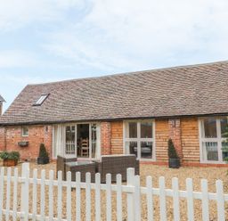 A single story house with brick and wood exterior a gravel yard outdoor furniture and a white picket fence at Megs Cottage in Tiddington
