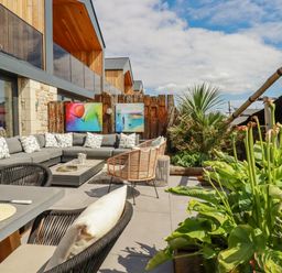 An outdoor patio with a sectional sofa dining table chairs plants and modern artwork at Stargazers in Sennen