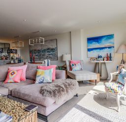 A living room with a gray sectional sofa with colorful pillows a patterned armchair a chaise lounge and artwork on the walls at Stargazers in Sennen