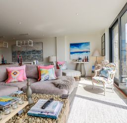 A living room with a sectional sofa and colorful cushions beside glass doors at Stargazers in Sennen