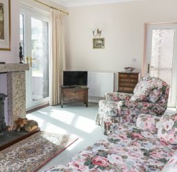 A living room with floral upholstered sofa and armchair a wood burning stove and a small television at Sheilas Cottage in Penryn
