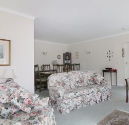 A living room with floral sofas a dining table with chairs a bookcase and framed pictures at Sheilas Cottage in Penryn