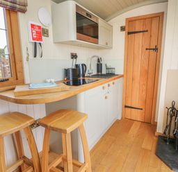 A small kitchen with wooden stools wooden countertop stove and wood burning stove at Ivys Way in Rhayader