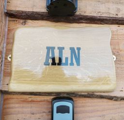 A wooden plaque with the letters ALN mounted on a wooden wall with a doorbell below at Aln in Longframlington
