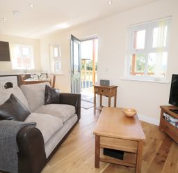 A living room with a sofa coffee table television and kitchen area visible at Aln in Longframlington