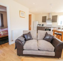 A living area with a two-seater sofa and an open kitchen with a dining table and chairs at Aln in Longframlington