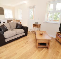 A living room with a sofa coffee table television and kitchen in the background at Breamish in Longframlington