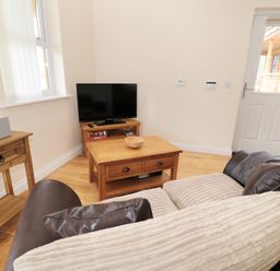 A living room with a couch a wooden coffee table a television on a wooden stand and a side table at Breamish in Longframlington