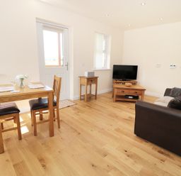 A living area with wooden dining table and chairs a sofa wooden TV stand and side table at Breamish Longframlington