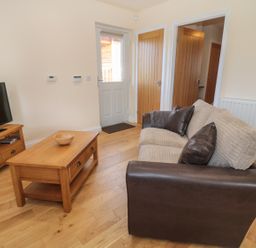 A living room with a brown and beige sofa wooden coffee table wooden tv stand and a television at Breamish in Longframlington