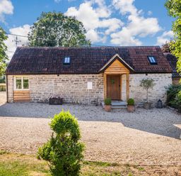 A stone house with a tiled roof and a wooden door surrounded by gravel and plants at Old Farm Stables South Barrow near Sparkford