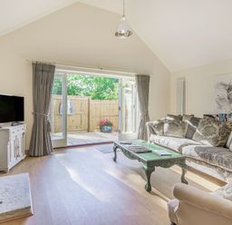 A living room with a sofa an armchair a coffee table a television and glass doors opening to a fenced garden at Old Farm Stables South Barrow near Sparkford