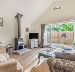 A living room with sofas a coffee table a wood stove TV and large sliding doors at Old Farm Stables South Barrow near Sparkford
