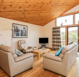 A living room with beige sofas a wooden coffee table a tv and wooden ceiling at Burnside Lodge in Aberfeldy