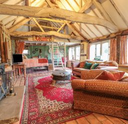 A living area with sofas a wood stove a bed and wooden beams at Jackdaw's Roost in Cheltenham