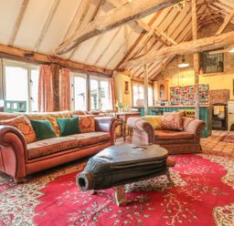 A living room with wooden beams a sofa armchair and a coffee table on a red rug at Jackdaw's Roost in Cheltenham