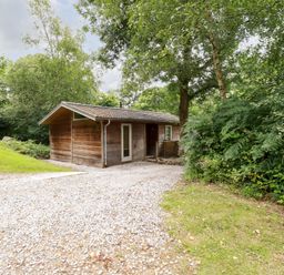 A small wooden cabin surrounded by trees and bushes with a gravel driveway at 4 Stonerush Valley Lanreath