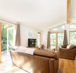 A living room with brown leather sofas a wooden coffee table a television and large windows at 7 Streamside in Lanreath