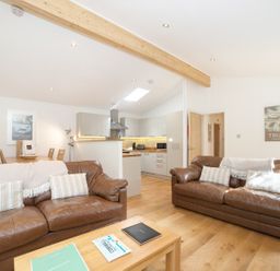 An open living room with two brown leather sofas and an adjoining kitchen at 7 Streamside in Lanreath
