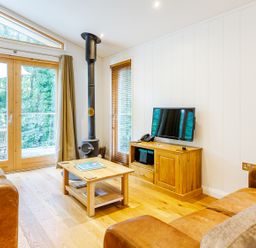 A living room with two brown leather sofas a wooden coffee table a wood burning stove and a TV on a wooden cabinet at 8 Streamside in Lanreath
