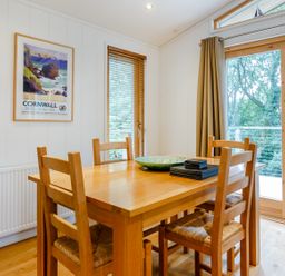 A dining area with a wooden table and four chairs near windows and glass doors at 8 Streamside in Lanreath