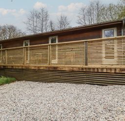 An exterior view of a wooden house with horizontal slatted railings and gravel ground at 2 Stonerush Valley in Lanreath