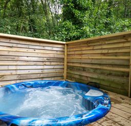 An outdoor hot tub with blue and white swirls surrounded by wooden fencing and trees at 2 Stonerush Valley in Lanreath