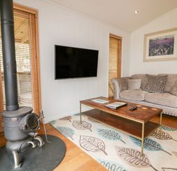 A living room with a wood stove a wall-mounted TV a sofa and a coffee table at 9 Stonerush Valley in Lanreath