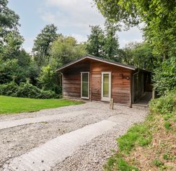 A wooden cabin with glass doors and a gravel driveway surrounded by trees and grass at 9 Stonerush Valley in Lanreath