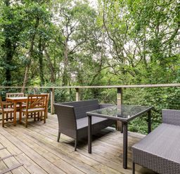 An outdoor wooden deck with two seating areas surrounded by trees at 9 Stonerush Valley in Lanreath