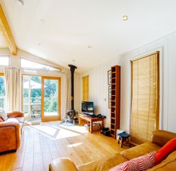 A living room with leather sofas wooden floor wood stove and a television at 2 Water's Edge in Lanreath