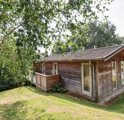 A wooden cabin with a small balcony surrounded by grass and trees at 2 Water's Edge in Lanreath