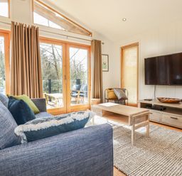 A living room with a blue sofa pillows wooden coffee table wall mounted TV and large windows at 4 Water's Edge in Lanreath