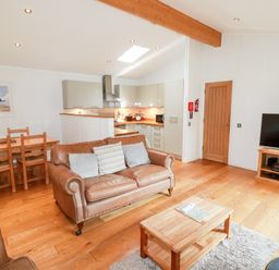 An open living room with leather sofas a wooden coffee table a dining table a kitchen area and a television at 6 Water's Edge Lanreath