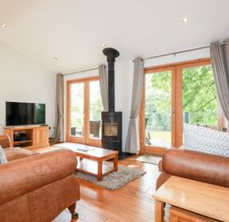 A living room with leather sofas a coffee table a stove and a television at 6 Water's Edge in Lanreath