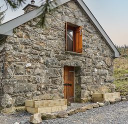 A small stone building with a wooden door and an open wooden window with planters outside at Brithgwm Canol in Brithdir near Dolgellau