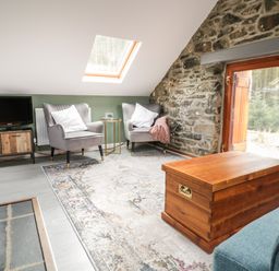 A sitting area with two armchairs a wooden chest a TV on a stand and a stone wall at Brithgwm Canol in Brithdir near Dolgellau
