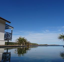 An outdoor pool with a house on the left and plants near the pool overlooking hills and ocean at The Sandcastle in Freshwater East
