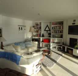 A living room with sofas cushions bookshelf and a television at The Sandcastle in Freshwater East