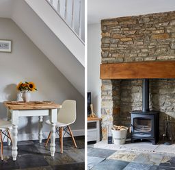 A dining area with a wooden table and two chairs under a staircase and a stone fireplace with a wood burning stove and firewood in a bucket at Lilly Cottage in Whitecroft Royal Forest of Dean