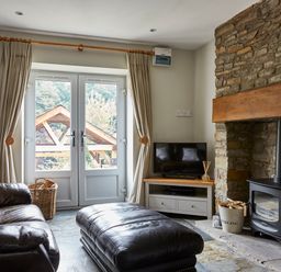 A living room with leather sofa and ottoman a wood burning stove and a television at Lilly Cottage in Whitecroft Royal Forest of Dean