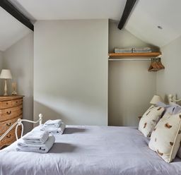 A bedroom with a bed folded towels and pillows a dresser with a lamp and mirror and an open closet with hangers at Lilly Cottage Whitecroft Royal Forest of Dean