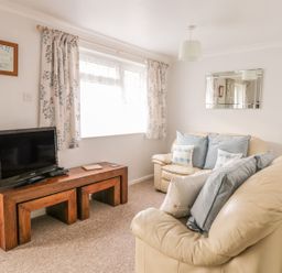 A living room with cream sofas blue cushions a wooden table with a tv and floral curtains at Ducks Ditty in Liskeard