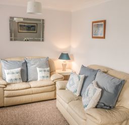 A living room with two beige leather sofas multiple cushions a side table with a lamp a wall mirror and framed pictures at Ducks Ditty in Liskeard
