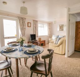 A dining area with a round table set for four and a living room with beige sofas and a TV at Ducks Ditty in Liskeard