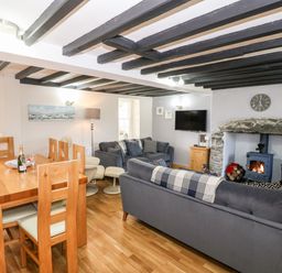 A living room with gray sofas a stone fireplace and a wooden dining table at Min-y-rhos in Edern